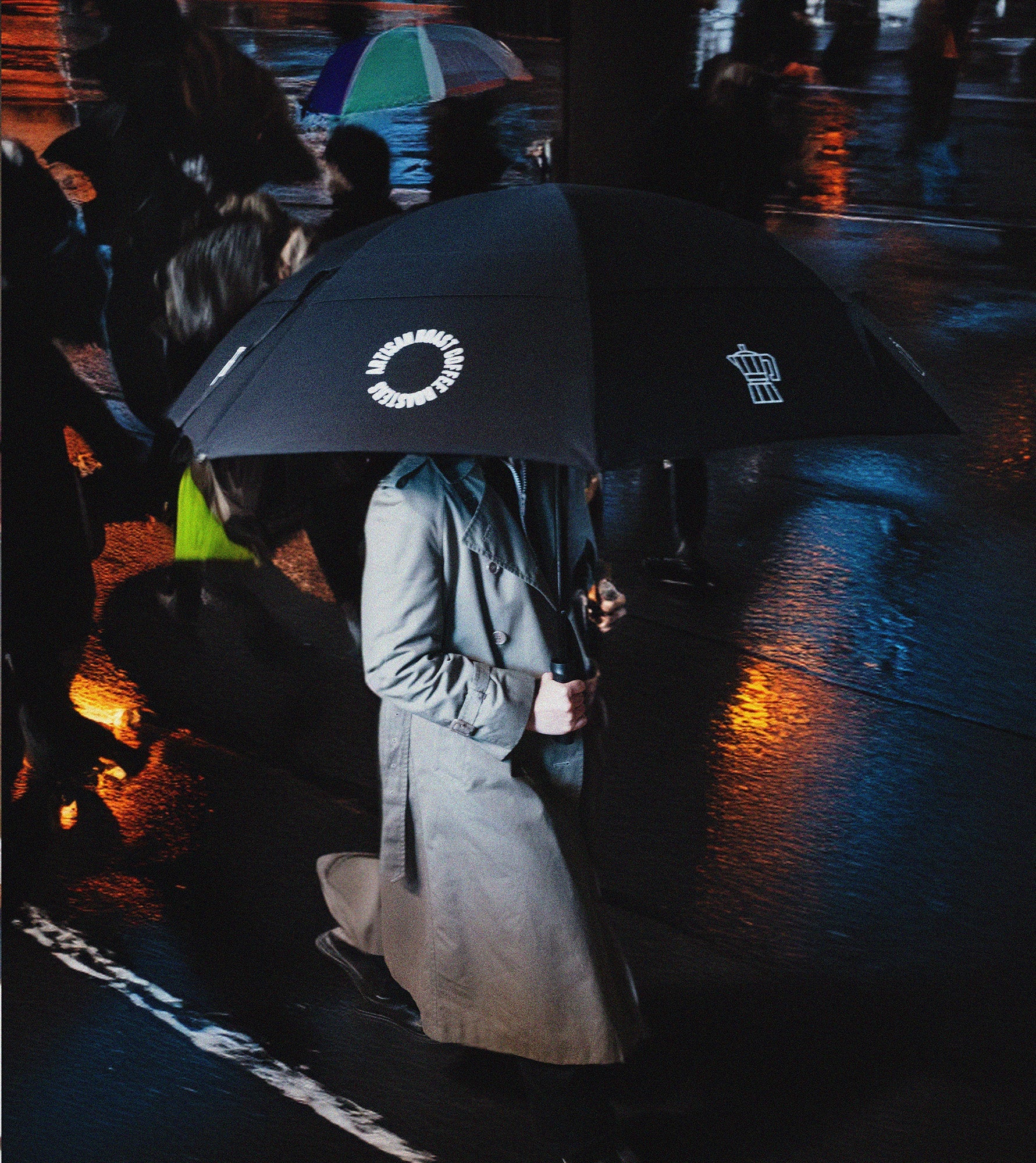Person holding a black umbrella with visible branding on a rainy street.